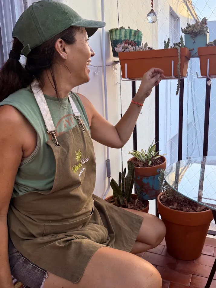Pau, de Verdetucci, con su delantal cuidando las plantas de su balcón